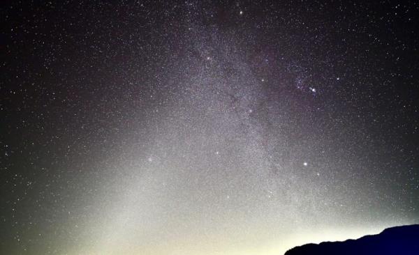 Two fuzzy bands of light shining up from horizon into the starry sky, 1 the Milky Way and 1 the zodiacal light.